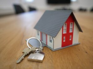 A set of keys next to a miniature wooden house.