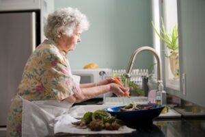 An older woman wearing an apron, washing vegetables in the kitchen