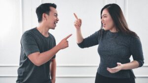 Two siblings in dark clothes arguing and pointing fingers at each other