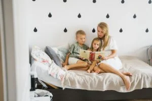 A mother with two small kids sitting on a bed next to a white wall 