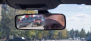 A man looking in the rearview mirror to prevent back-up accidents.