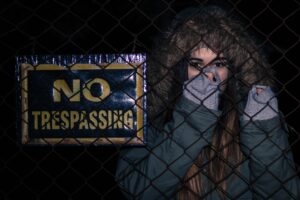  a woman holding onto a fence with a “No Trespassing” sign