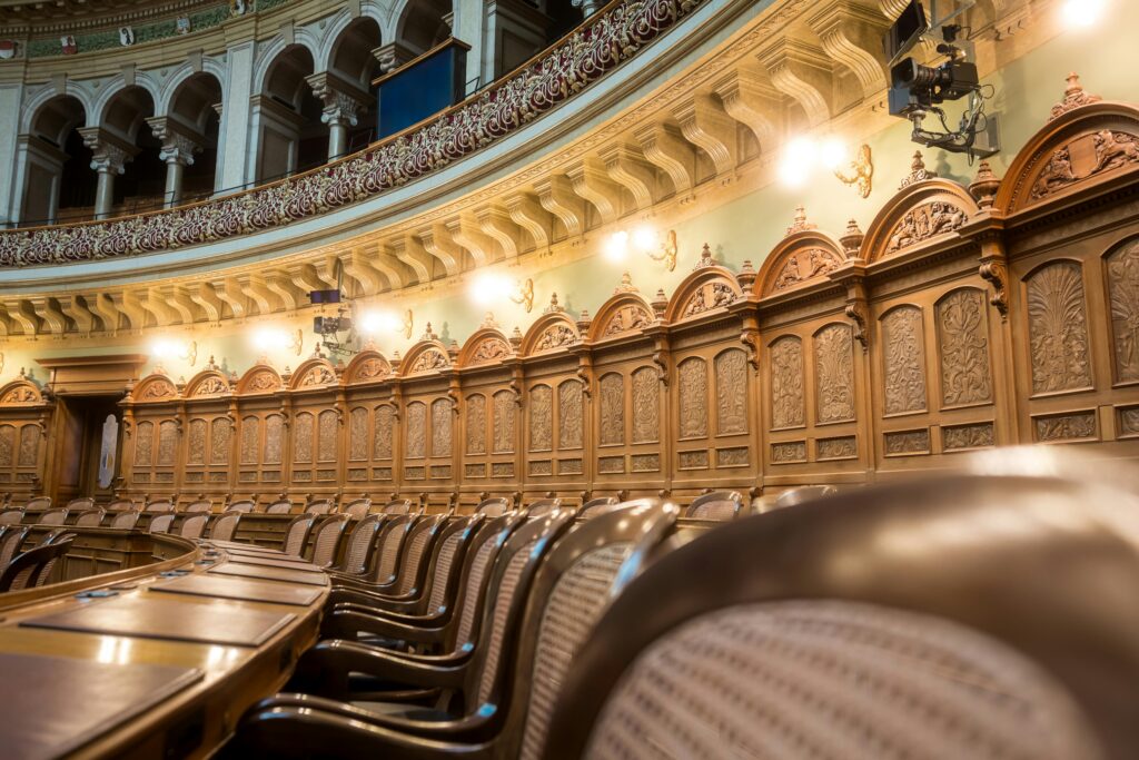 Interior of a historic theater with carved wooden panels along the walls, rows of seats, and an ornate balcony railing above